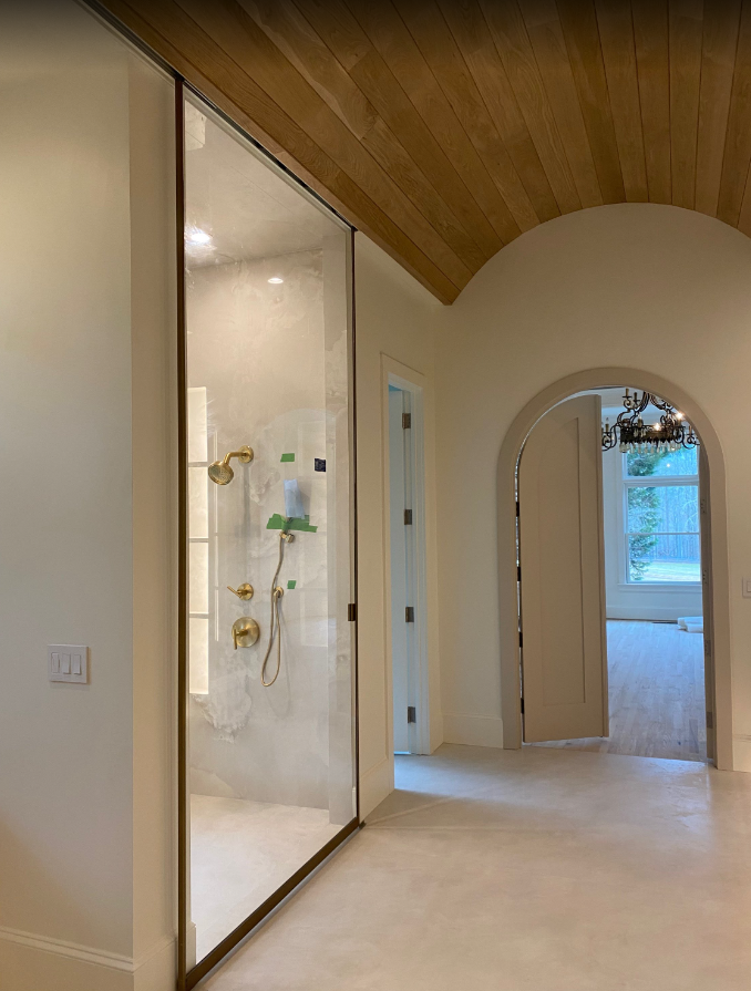 The large panel took 4 installers to lift into the ceiling! The slider bar was actually installed into the ceiling ahead of time while the glass was being fabricated. We wrapped the panel in a custom gold frame, and it slides from the shower to the vanity/makeup room next door. Ask us about your custom glass partition!